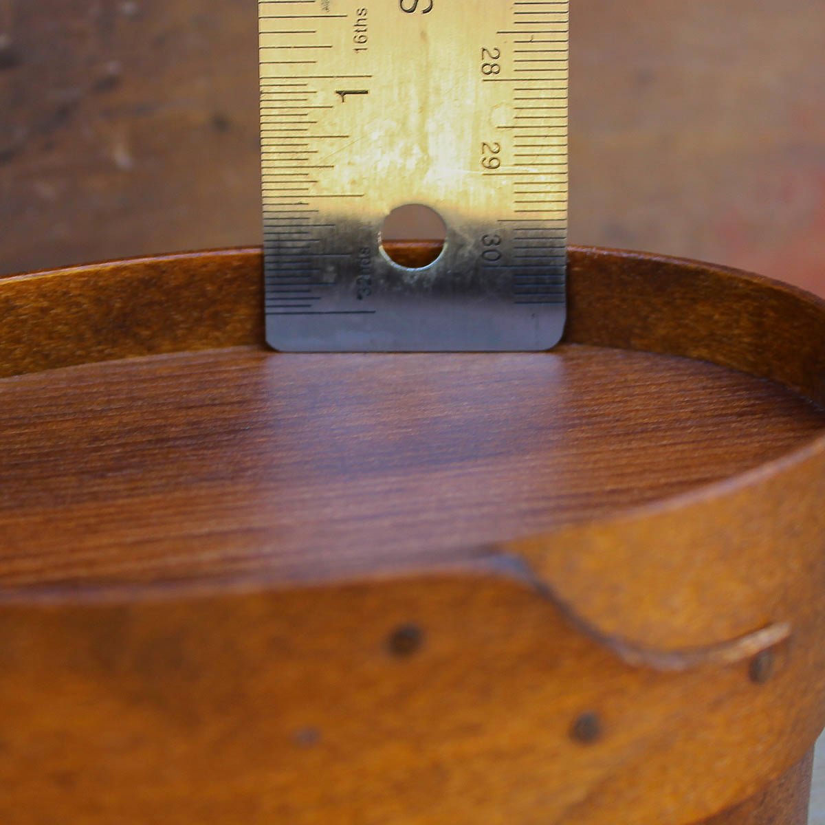 Close-up of a handcrafted oval Shaker box from Maine, with a ruler measuring its height for sewing box enthusiasts.
