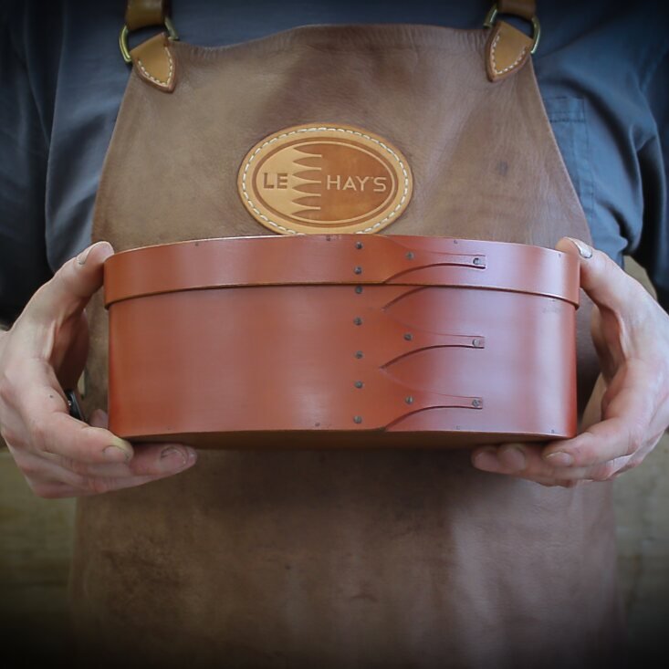 Handcrafted wooden shaker box from Maine, perfect for sewing and needlework, held by a person in a leather apron.