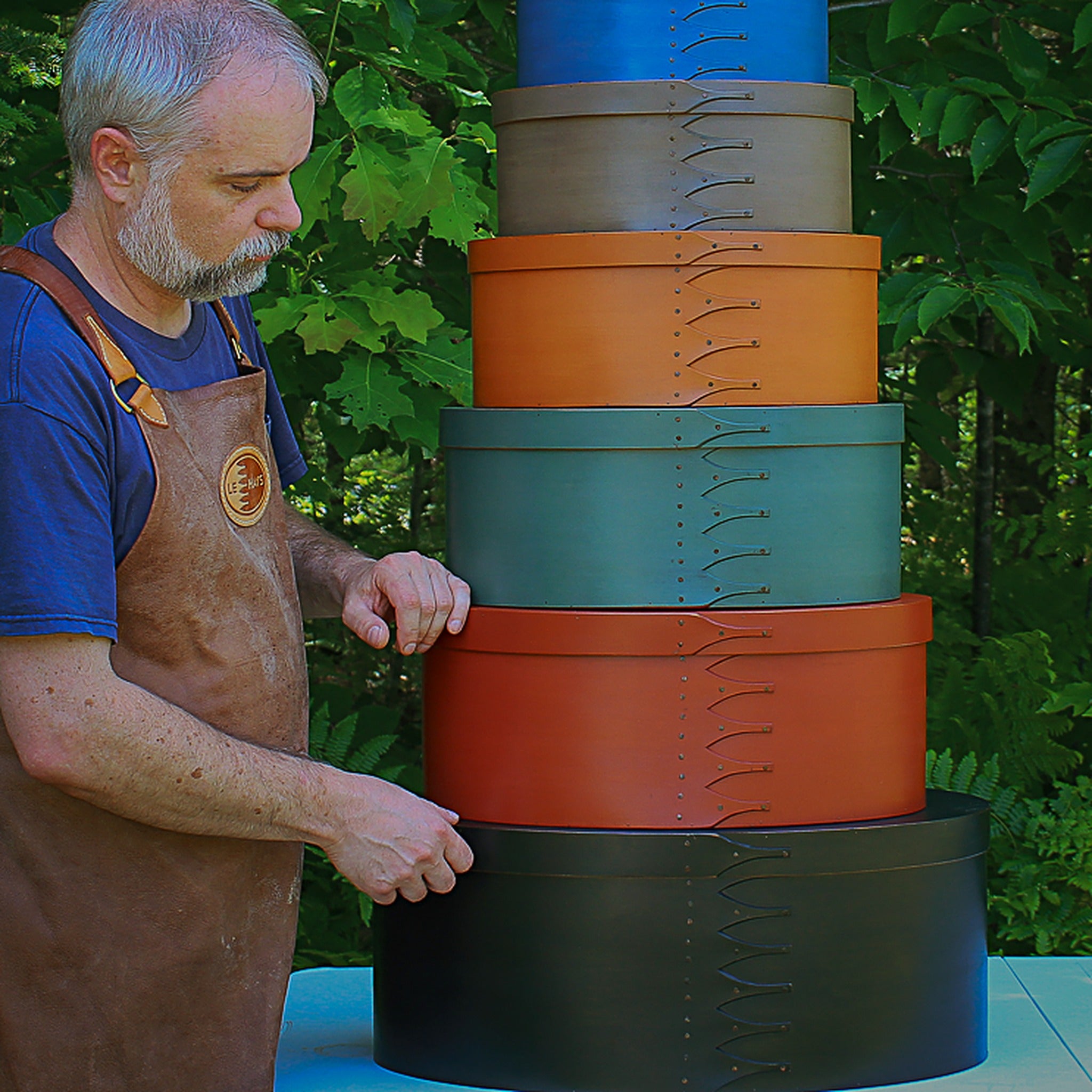 Rob LeHay assembling a tall stack of Shaker oval boxes in mixed milk paint colors — LeHay's Shaker Boxes