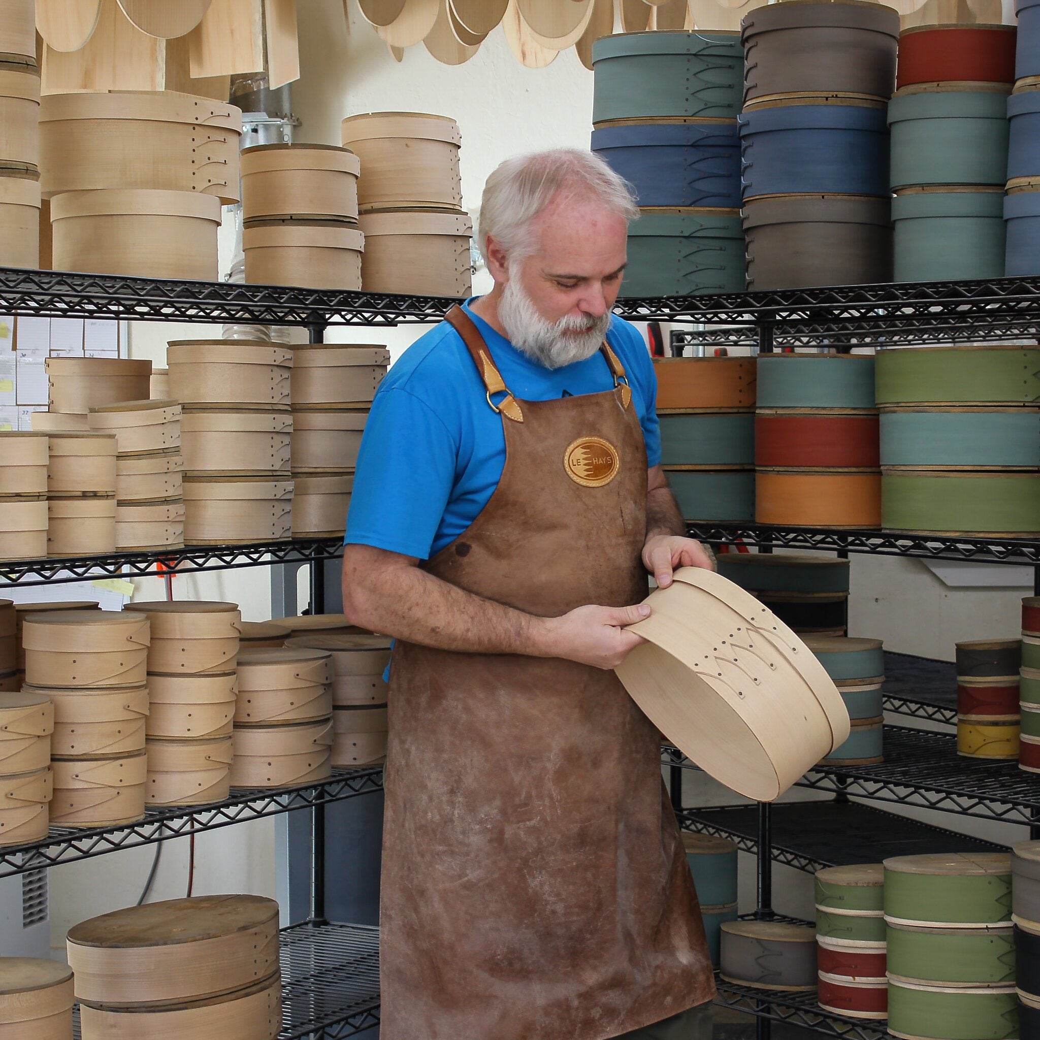 Craftsman inspecting handcrafted wooden shaker boxes in a workshop, showcasing handmade sewing and needlework boxes.