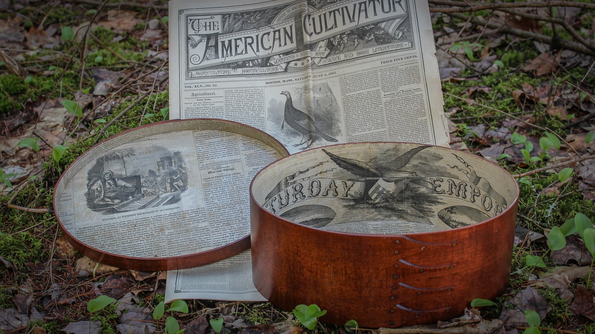 Handcrafted wooden oval shaker box from Maine with sewing supplies, resting on an antique newspaper.